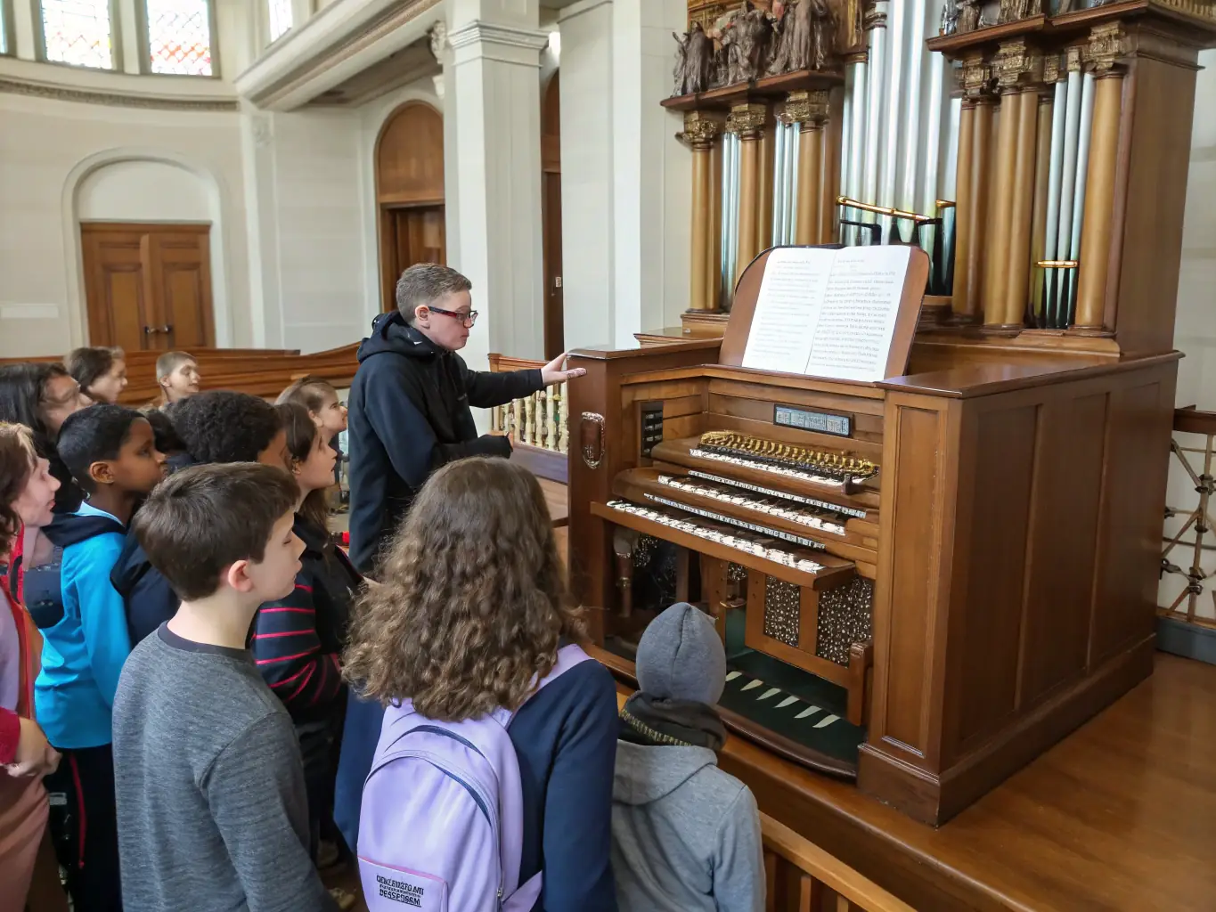 A diverse group of people attending a lecture on organ music history, with a projector displaying historical images and musical scores.